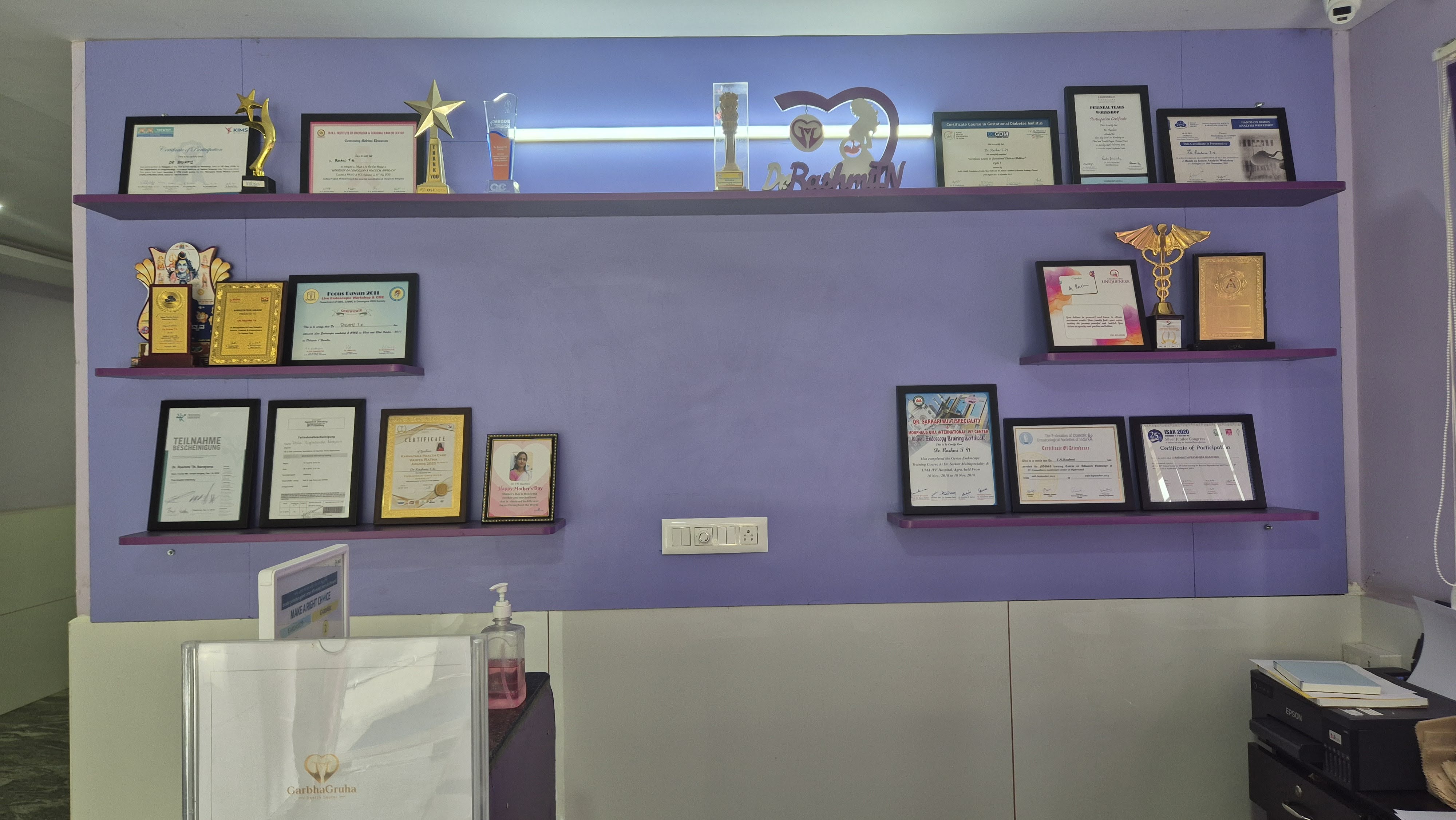 Awards wall at GarbhaGruha Health Center — trophies, certificates and Dr. Rashmi T N recognition display